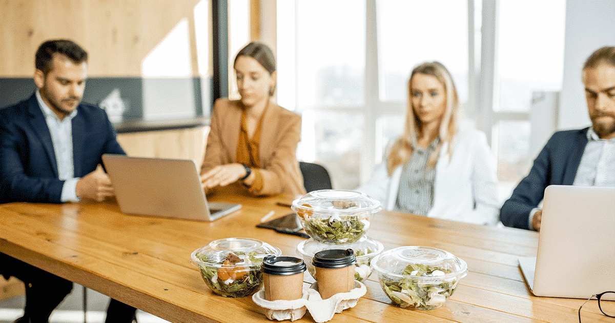 Office table with salads, drinks an four people in the background